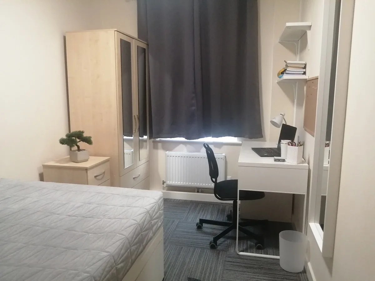 A furnished student bedroom with a bed, desk, chair and wardrobe