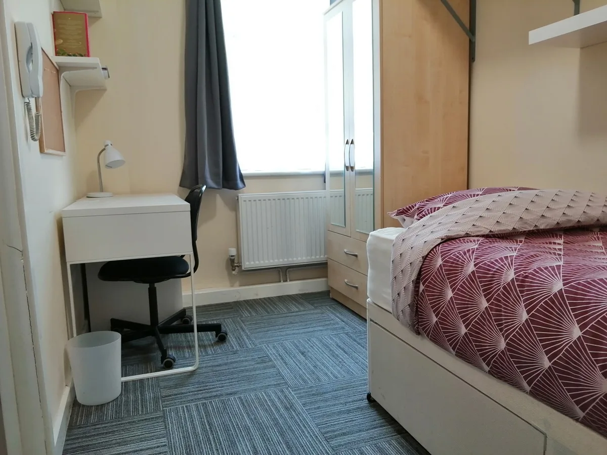 A student bedroom with a double bed, desk and reading lamp