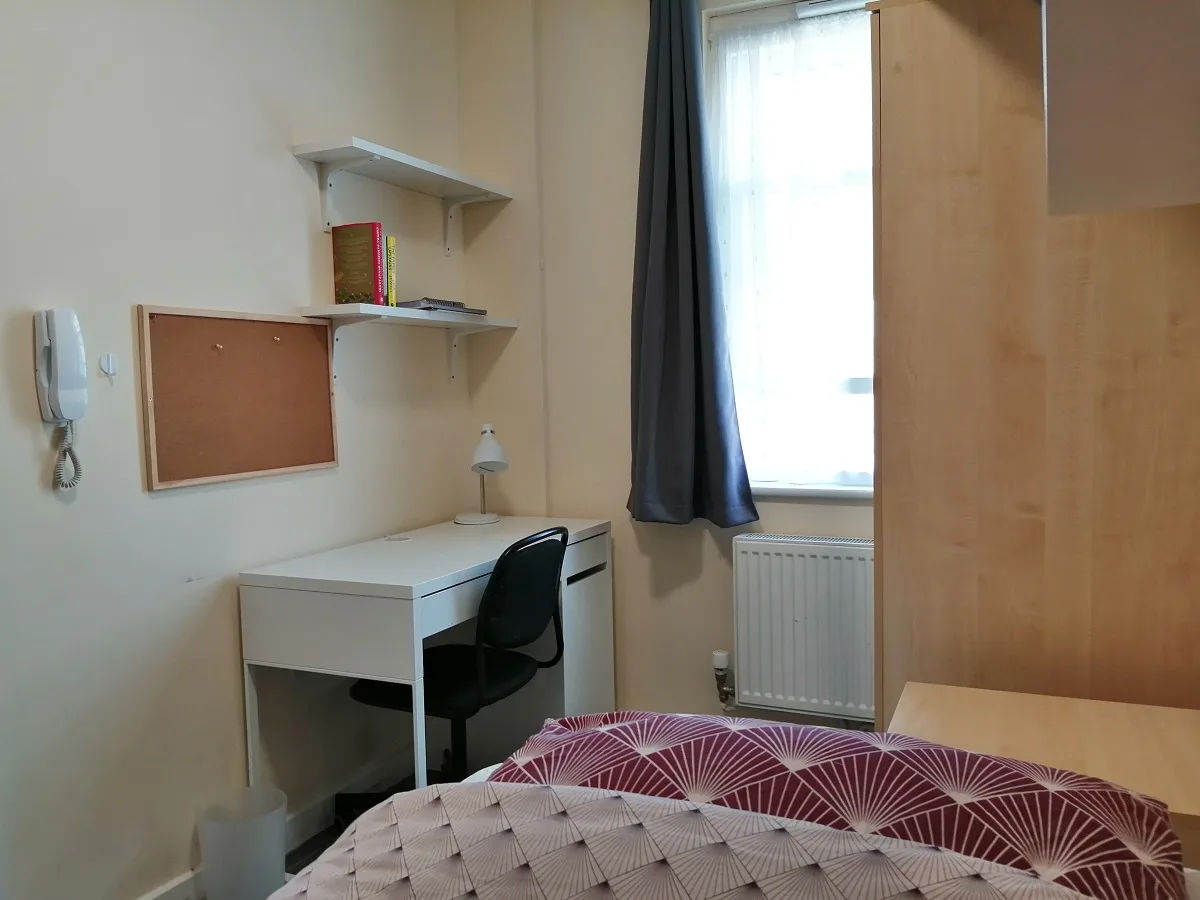 A student bedroom with a desk, shelving and a double bed