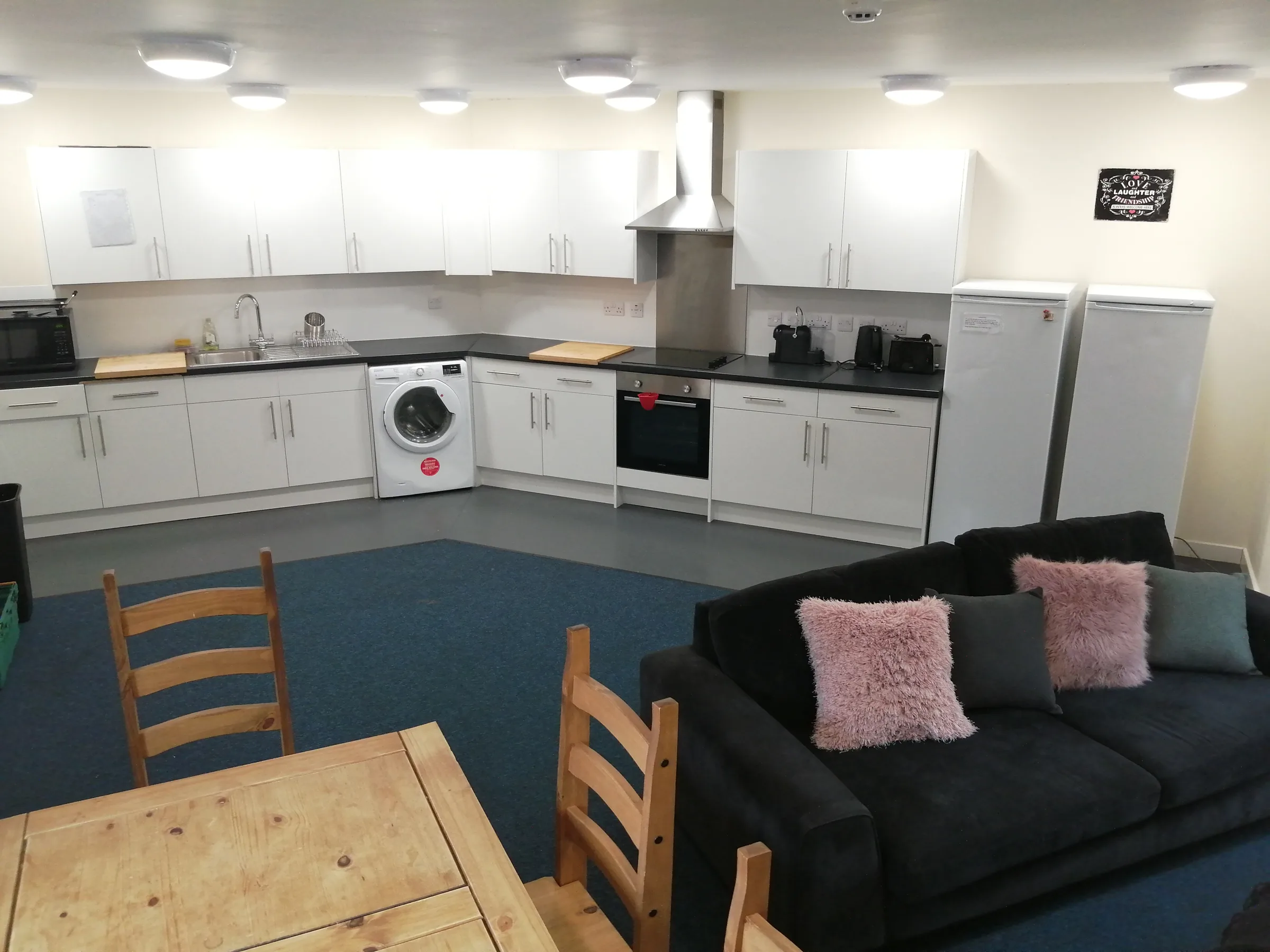 An apartment kitchen and lounge with integrated appliances, a sofa and a dining table
